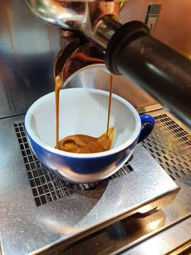 Barista pouring latte art into a small ceramic cup